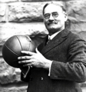 Mann im Anzug hält einen Basketball vor einer Steinmauer.